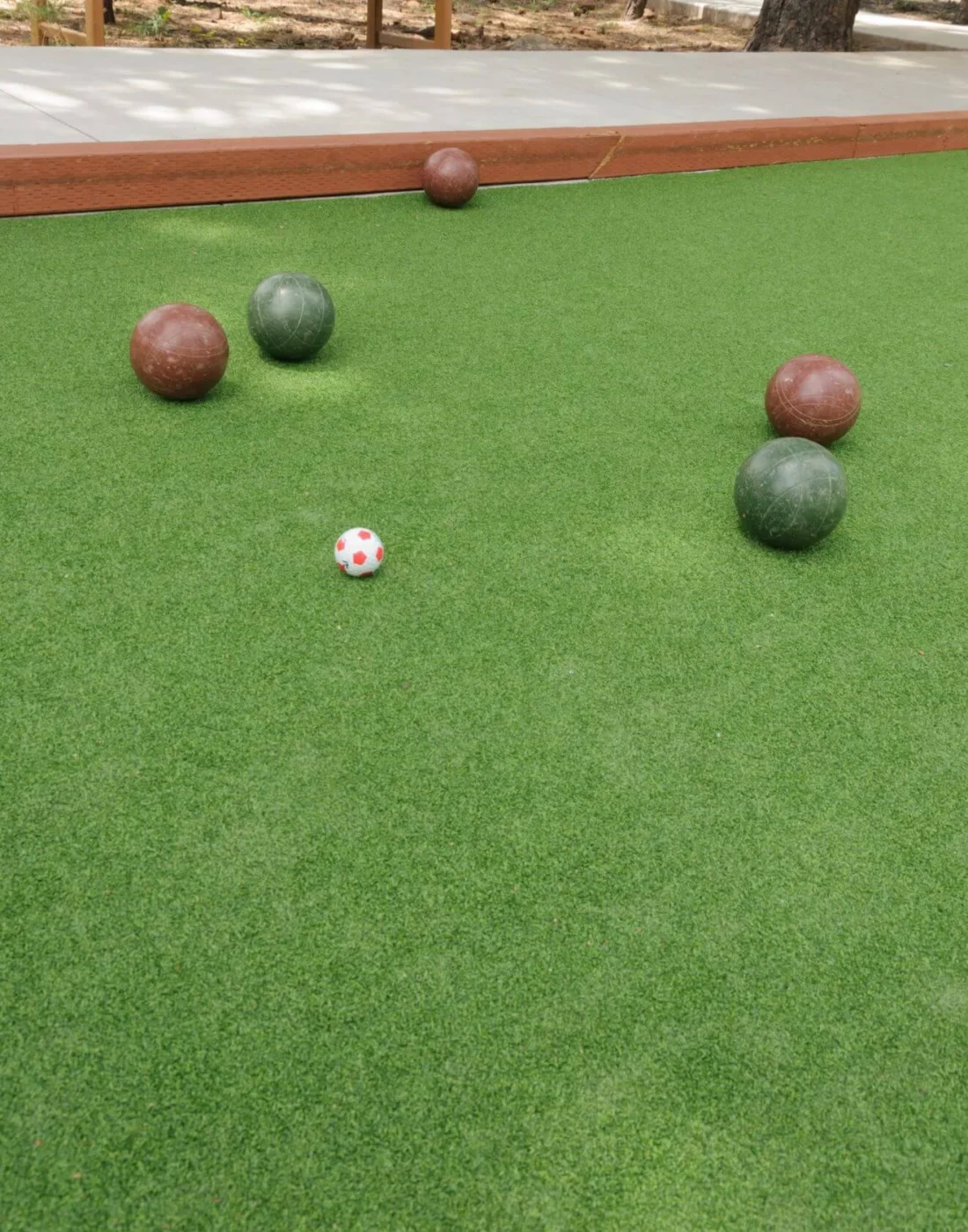 Bocce balls on a lush green outdoor court with several red and green balls scattered about the small target ball at the center. The well-maintained ABQ Turf enhances play, while a wooden boundary frames this delightful scene in Albuquerque, NM.